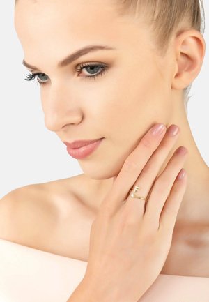 Gold rings featuring a minimalist design; one has a capital "F" accent and the other includes a small gem. Smooth surface, polished finish.