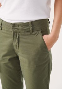 Pantalons en coton vert olive avec une coupe droite, dotés de poches latérales et d'une texture lisse. La ceinture présente des détails de couture subtils.