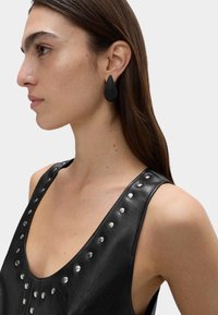 Pendientes en forma de lágrima negros con una textura estriada. El modelo lleva una blusa sin mangas negra acentuada con tachuelas plateadas.