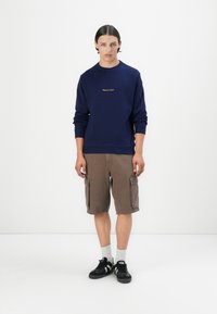 Sweatshirt bleumarin cu manșete și tiv cu nervuri, asociat cu pantaloni scurți cargo căprui, cu buzunare laterale și croială lejeră, adidași negri.