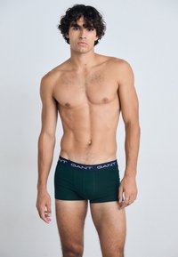 Zöld pamut boxer alsónadrág sötétkék derékkal, amelyen a "GANT" logó található. Az illeszkedés kényelmes, designja pedig egyszerű, minta nélkül.