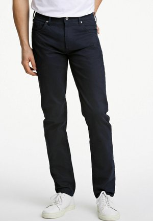 Pantalons en coton bleu marine à coupe droite, avec poches avant, fermeture éclair et bouton. Portés avec des baskets blanches.