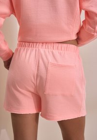 Shorts roses texturés avec une taille élastique et une seule poche arrière. Le tissu présente un petit motif en relief.