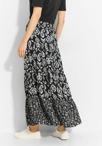 Jupe maxi noire ornée de motifs blancs complexes, avec un design à étages et un ourlet volanté. Portée avec des baskets blanches.