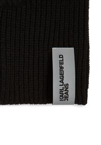 Juodas megztas audinys su tekstūru, turintis pilką etiketę su įspaustu užrašu "KARL LAGERFELD JEANS" juoda spalva.