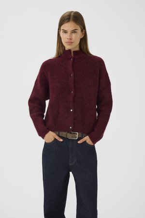 Burgundy wool cardigan with a high neck, button front, and long sleeves; paired with high-waisted dark denim pants and a tan belt.