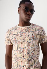 Kortærmet t-shirt lavet af bomuld med et flerfarvet abstrakt geometrisk mønster i røde, gule, sorte og cremefarvede nuancer, rund halsudskæring.
