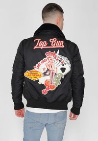 Svart bomberjacka med "Top Gun" broderi, livfulla lappar med en pin-up tjej, spelkort och Las Vegas-skyltar i flera färger.