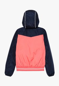 Bunda větruodolná s kapucí, navy modré a korálové barvy, elastickými manžetami a páskem se proužky. Hladký, lehký nylonový materiál.