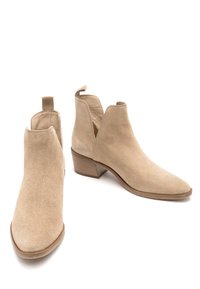 Beżowe zamszowe botki za kostkę z ostrym noskiem, niskim obcasem słupkowym i wyciętymi bokami. Minimalistyczny design z gładką teksturą.
