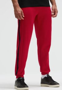 Rote Sporthosen aus glattem Stoff mit schwarzen Seiteneinsätzen, die den Text "CAMP DAVID" tragen, enganliegendes Design mit gerippten Knöcheln.