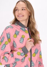Jachetă bomber roz cu model de ananas, având accente verzi și guler gri. Închidere cu fermoar în față și manșete elastice. Material ușor.