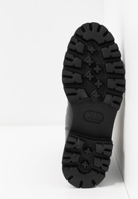 Schwarze Gummilaufsohle mit tiefen Profilen, die hexagonale und sternförmige Muster aufweist. Robustes Design mit verstärktem Rand.