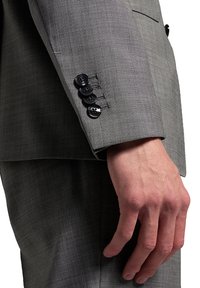 Nahaufnahme einer Hand neben dem Ärmel eines grauen Sakkos mit vier schwarzen Knöpfen.