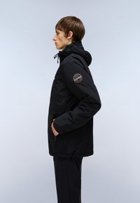 Svart huva jacka med dragsko, sidofickor och en patch på vänster ärm. Tyg med en slät, matt textur.