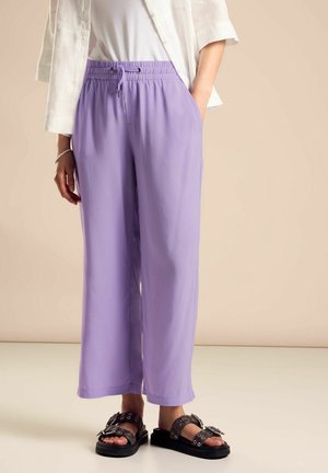Person wearing lilac wide-leg pants with an elastic waistband and black buckle sandals against a beige background.