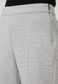 Hlače iz tkanine s srebrno herringbone vzorcem, z gladko teksturo, naravnega kroja in pasom brez vidnih zaponk.