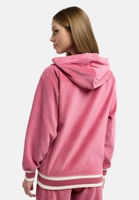 Rosa huvtröja i mjukt tyg, med avslappnad passform, ribbade muddar och kontrasterande vita ränder vid midjan och ärmarna.