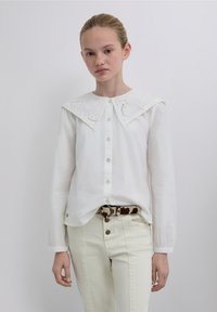 White button-up shirt with a large, detailed embroidered collar, long sleeves, and a relaxed fit, paired with light-colored jeans and a patterned belt.