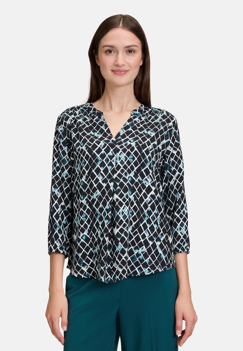 Blouse à motifs noir et blanc avec des manches trois-quarts et un col en V. Présente un design géométrique avec des accents de turquoise et de blanc.