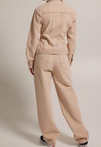 Beige denimjacka med matchande vida byxor, med insvängd midja, bakfickor och knappade ärmslut. Texturen verkar mjuk och robust.