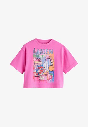 Camiseta de manga corta rosa con un gráfico colorido que muestra una jarra, una porción de pastel, frutas, ajo y el texto "GARDEN PARTY" en el frente.