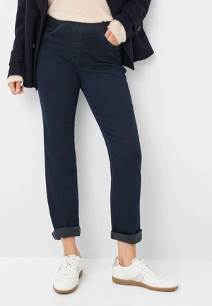 Pantaloni in denim blu scuro, taglio dritto con orli arrotolati, dotati di tasche laterali e una texture liscia, abbinati a sneakers bianche.