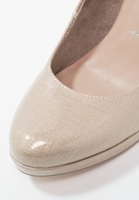 Chaussure à talon haut beige avec une finition brillante et un motif texturé. Bout arrondi et doublure intérieure douce, mettant en valeur un éclat subtil et une élégance.