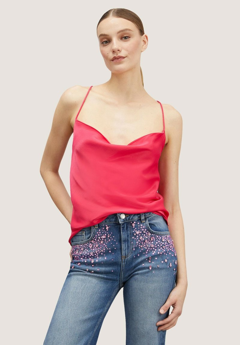 Fuchsia Satin-Camisole mit dünnen Trägern, kombiniert mit hellblauen Jeans aus Denim, die mit einer rosa Perlenverzierung an den Taschen versehen sind.