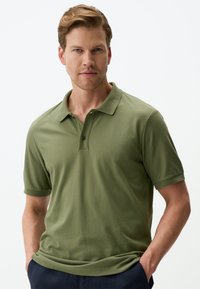 Polo shirt verde oliva realizzato in morbido tessuto, con colletto, maniche corte e patta con due bottoni. Texture semplice e liscia.
