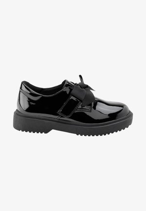 Chaussure en cuir verni noir avec semelle en caoutchouc épaisse et large ruban noir noué en un nœud sur le dessus.