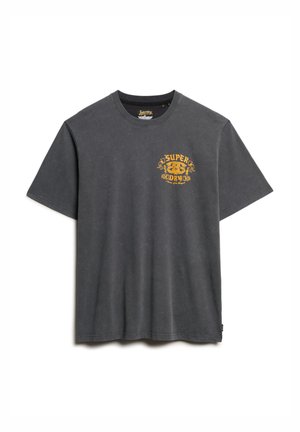 Camiseta de algodón en gris oscuro con cuello redondo. Presenta un diseño gráfico dorado en el lado izquierdo del pecho. Mangas cortas y ajuste relajado.