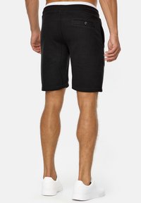 Shorts de sport noirs en tissu doux, dotés d'une poche arrière avec un bouton, d'une taille élastique et de baskets blanches assorties.
