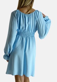 Abito azzurro chiaro con vita arricciata e smock, maniche lunghe a sbuffo e scollatura rotonda. Realizzato in un morbido tessuto testurizzato.