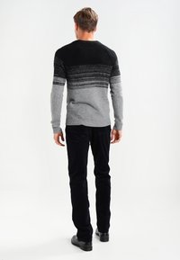 Šedý a černý pruhovaný pletený svetr s kulatým výstřihem, texturovaná tkanina, v kombinaci s černými sametovými kalhotami a černými botami, pohled zezadu.