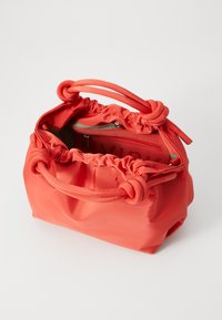 Orange nylonhandväska med samlade kanter och knutna handtag. Har en blixtlåsförsedd innerficka och en mjuk, strukturerad yta.