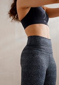 Melnā sporta krūšturis un augstiem vidukļiem paredzētas legingi ar reljefu, rakstainu dizainu tumšās zilā un zaļā nokrāsās. Gluda auduma, pieguļošs stils.