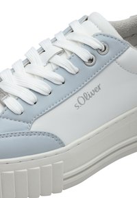 Biele a svetlomodré tenisky s textúrovaným koženým zvrškom, plochými bielymi šnúrkami a hrubou, vrúbkovanou bielou gumenou podrážkou.