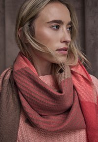 Strikket tørklæde med et gradientdesign i nuancer af koral og brun, med et tekstureret mønster og blød finish, viklet rundt om halsen.