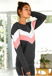 Sudadera negra con patrón de chevrón rosa y blanco, cuello redondo, mangas largas y puños acanalados; combinada con pantalones negros.