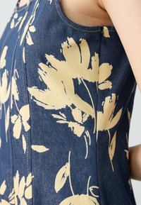 Denim-Oberteil mit einem dunkelblauen Hintergrund und großen gelben Blumenmustern, einer figurschmeichelnden Passform und einem sichtbaren seitlichen Reißverschluss.