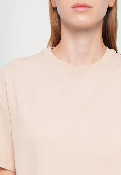 Short-sleeve, crew-neck T-shirt made of smooth, soft fabric in light beige, featuring simple stitching details around the neckline.