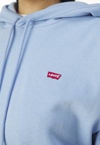 Hoodie bleu clair en coton avec une finition texturée. Il présente un petit logo Levi's rouge sur la poitrine et des cordons de serrage réglables.