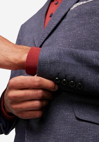 Granatowa strukturalna marynarka z kontrastową bordową koszulą pod spodem. Posiada cztery czarne guziki na mankietach oraz wzorzysty poszetkę.
