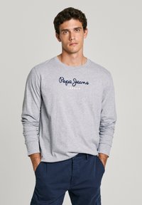 Szürke, hosszú ujjú póló, amelyen kék írott betűkkel szerepel a "Pepe Jeans London" felirat. Az anyag lágy tapintású, a minta kerek nyakkivágású.