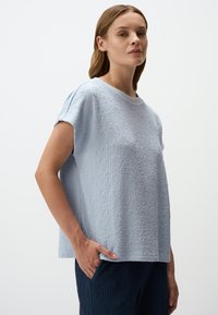 Jasnoniebieski T-shirt z krótkim rękawem i okrągłym dekoltem, o lekko luźnym kroju i subtelnymi, podniesionymi wzorami.