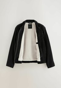 Zwart corduroy jasje met een witte pluche binnenvoering, voorzien van een voorrits en een standaard kraag. Label zichtbaar aan de binnenkant van de halslijn.