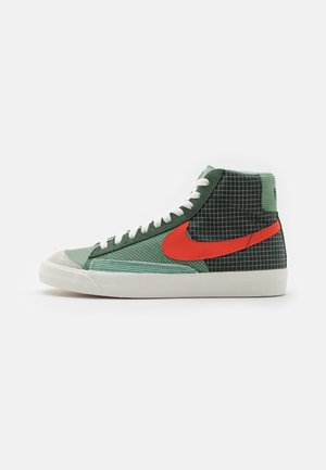 High-top sneaker in green shades with white laces, red Nike swoosh, black and white checkered fabric on heel, and white rubber sole.