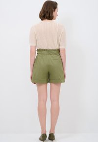 Maglione a maglia beige chiaro con maniche corte abbinato a pantaloni corti alta vita verde oliva con vita arricciata e tasca posteriore.
