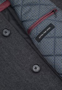 Szary wełniany płaszcz o fakturze jodełki, z czarnymi guzikami, pikowanym niebieskim podszyciem z ozdobnym wzorem oraz kieszenią na zamek z napisem "Extra Fine Wool".